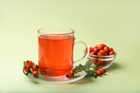Rosehip tea in cup and berries with leaves on light green background