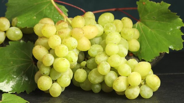 Bunch of fresh grapes with leaves on black table, closeup. Camera moving right