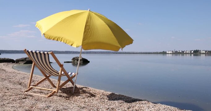 Yellow beach umbrella and deck chair by river. Camera moving right