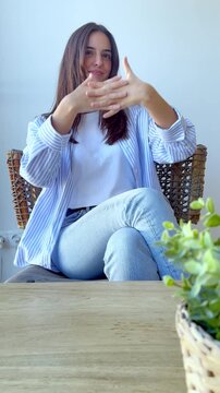 Young caucasian woman sitting at a wooden table, smiling and using hand gestures while talking, possibly during a casual interview, a vlog recording, or a relaxed conversation at home