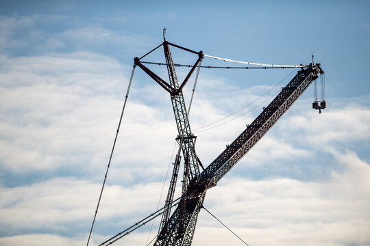 A modular jib crawler crane arm with a near-horizontal beam attached to a vertical mast or tower. The large inclined main boom mechanism and cable are empty from a load. The background is a cloudy sky