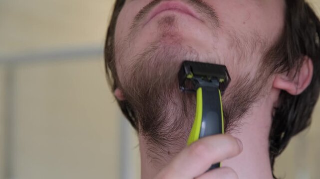 Man shaves beard in bathroom with electric razor during morning routine on a weekday