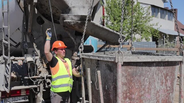 UKRAINE, May 4, 2026, Construction worker operates a concrete bucket beside a ready mix delivery truck at an active foundation site, A hardhat laborer controls the discharge chute while filling a