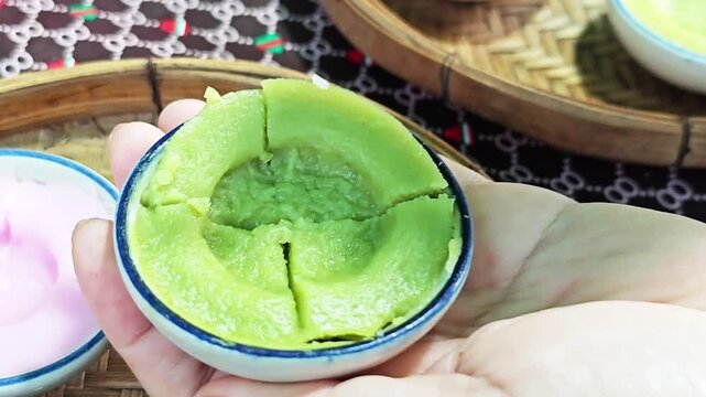 Pouring sweet brown sugar syrup over green pandan Thai steamed rice cake.