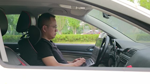 Man urgently works on his laptop inside car. He parks on the roadside and urgently uses his laptop to work.