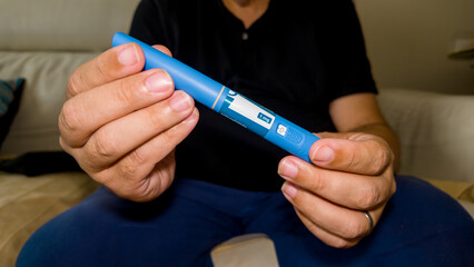Close up of a person seated on a white leather sofa inspecting a semaglutide GLP 1 subcutaneous pen device for diabetes therapy.