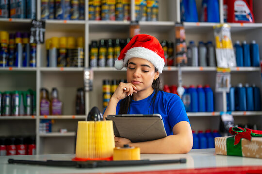 Female auto parts store employee wearing a santa hat checking inventory on a tablet