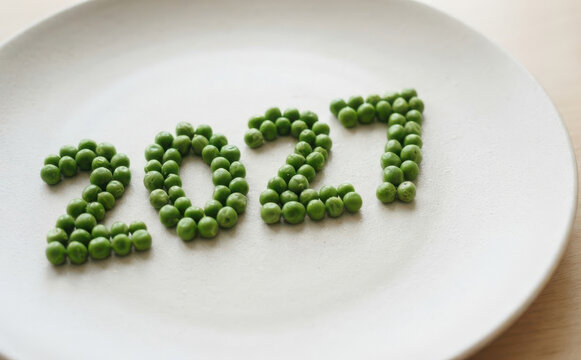Green peas arranged in the shape of the year twenty twenty one on a white plate representing the new year celebration and healthy eating concepts