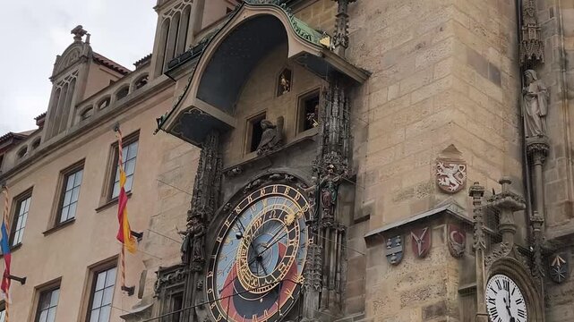Ornate Prague Astronomical Clock on historic building. Intricate golden details and moving celestial figures. Stone facade with carved statues and heraldic shields. Perfect for travel, history