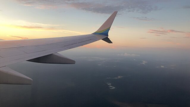 Airplane winglet silhouette against glowing orange sunset horizon from plane window
