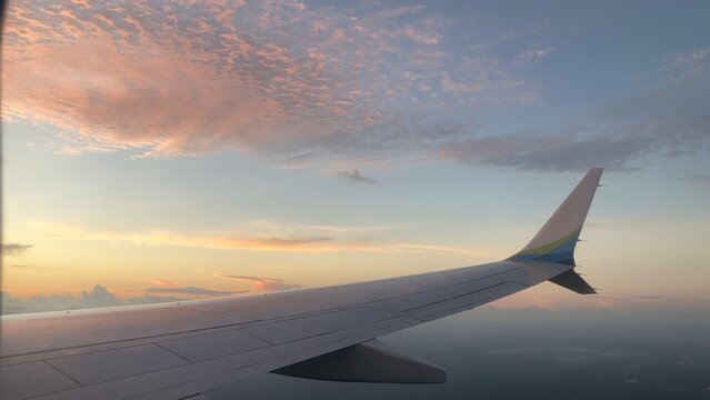View of airplane wing floating over soft pastel sunset clouds during flight