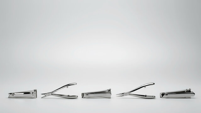 Five silver metal nail clippers and cuticle nippers arranged in a row against a clean white background with tools arranged horizontal horizontal line plain care