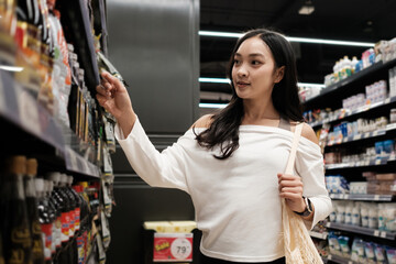 Obraz premium Asian woman shopping for groceries in supermarket aisle