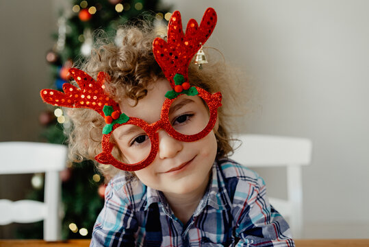 Portrait of a happy, young four year old boy wearing novelty glasses celebrating Christmas at home with his family in Australia