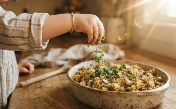 Little girl adding herbs to a homemade stuffing casserole dish for Thanksgiving dinner preparation in a rustic kitchen