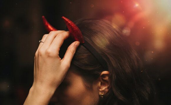 Young adult woman wearing red glitter devil horns headband for Halloween party concept close up portrait