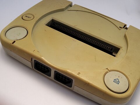 Isometric perspective of a dusty, yellowed 8-bit retro game console clone displaying front controller ports and a top cartridge slot
