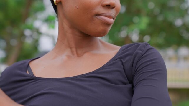 Close up view shows partial profile with soft focus background. subject is woman wearing dark clothing in outdoor park setting visible from her neck to mid chest area