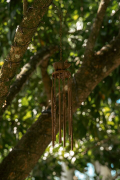A rusty metal wind chime with a pig figure hangs on a tree branch. Garden decor and backyard decoration. Metallic wind bells.