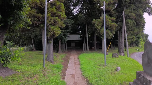 Slow walking POV through a stone torii gate towards a tranquil Shinto shrine in a green forest, Japan (Japanese text on the stone gate translates to the shrine's name and dedication details).