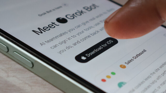 Finger pressing download for ios button on mobile phone showing grok bot app interface for digital work and productivity.