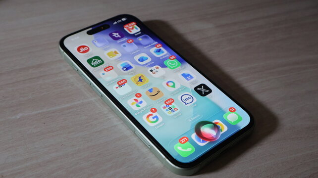 Handheld smartphone device showing active voice assistant animation over application grid on wooden textured surface.
