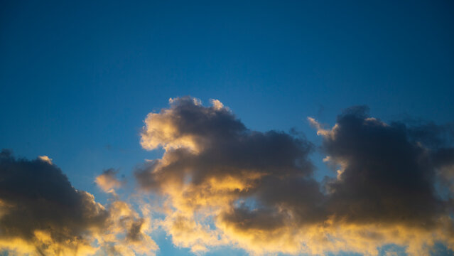 Dramatic sunset clouds illuminated by warm golden sunlight in a deep blue sky.
A stunning atmospheric photograph capturing a dramatic band of cumulus clouds drifting across a vibrant, deep blue sky 