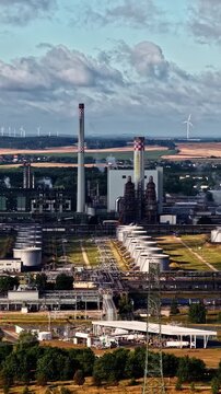 Schwedt, Brandenburg, Germany &ndash; The PCK Refinery Features Tall Smokestacks, Industrial Towers, Storage Tanks, And Pipelines, With Wind Turbines And Farmland In The Background &ndash; Aerial Drone Shot