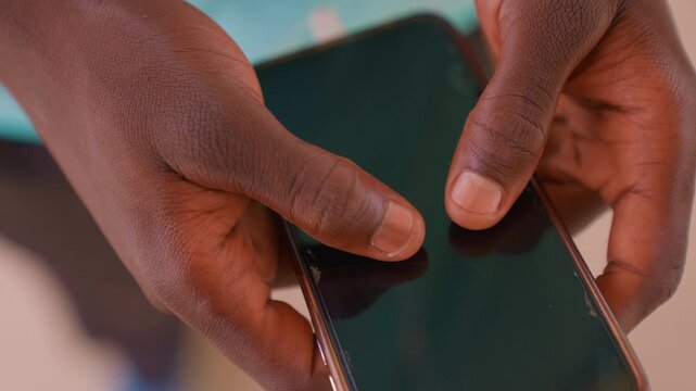 Close up shows two dark skinned woman hand holding damaged black screen phone. Hands grip device with visible skin details like lines and nails while background remains blurred emphasizing