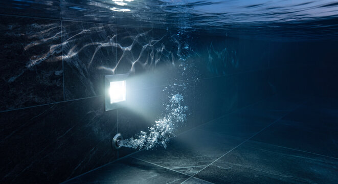 Bright square underwater pool light illuminating dark marble tiles and rising air bubbles