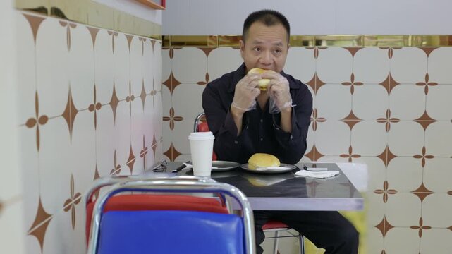 Man tries Hong Kong style pork chop bun for the first time. Man eats Chinese style burger. He wears disposable gloves while eating Chinese style burger.