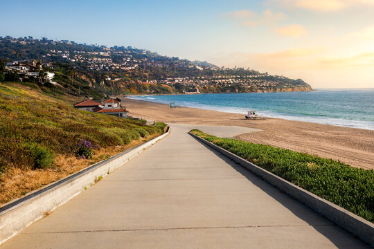 Scenic coastal road leading to a sandy beach with ocean views and hillside homes of Palos Verdes, California