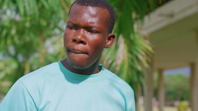 Close up view shows upper body and head of man wearing light blue shirt set against lush green foliage. subject remains in frame throughout with slight movements