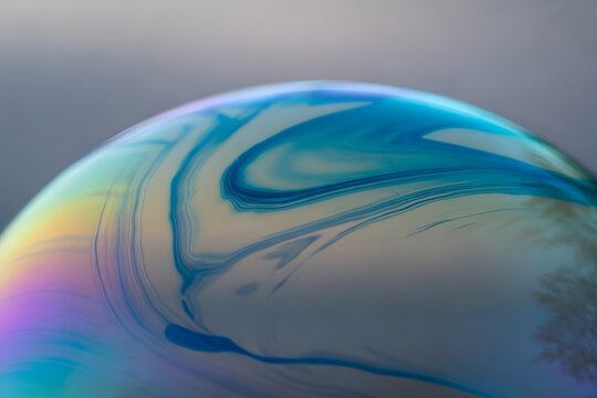Iridescent soap bubble macro, swirling blue and teal liquid patterns on spherical surface, abstract fluid art background with colorful oil film