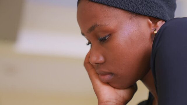 Close up shows right side facial features including ear with small hoop earring as person rests their head in their hands. background is softly blurred emphasizing soft lighting and calm