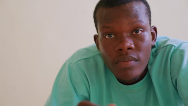 Man speaks and gestures while looking into camera wearing green shirt against plain background. His expressions change slightly as man communicates with consistent direct engagement
