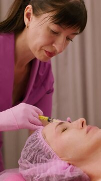 Vertical video. Beauty care. Aesthetic cosmetology. Female professional cosmetologist making botulinum toxin injection procedure for face skin treatment.