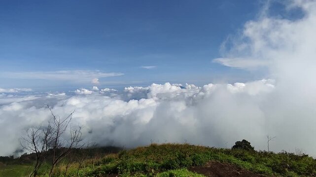 Sea of clouds over a mountain ridge on Mount Merbabu, viewed from the Thekelan hiking trail in Central Java, Indonesia, under a clear blue sky.