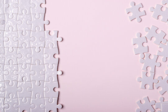 White jigsaw puzzle pieces connected on one side and scattered on soft pink background with copy space for text.