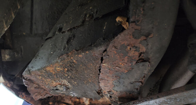 Rusted car floor pan with cracked metal, underside of an old vehicle
