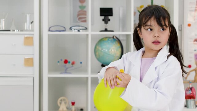 Young Girl in Lab Coat Inflating Yellow Balloon in Science Classroom