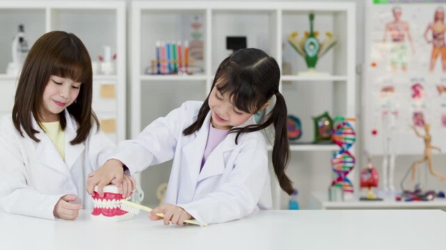 Asian Children in Lab Coats Learning Dental Hygiene with Tooth Model