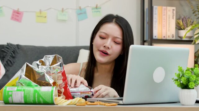 Tired Asian Woman Working on Laptop and Eating Snacks at Home