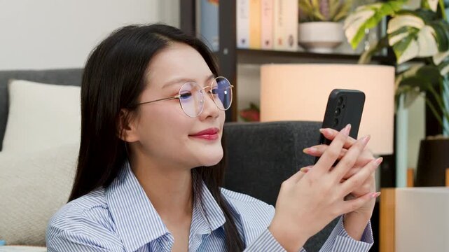 Young Asian Woman Smiling and Holding Smartphone in Living Room