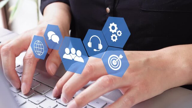 Close-up of hands typing on laptop keyboard. Blue icons float above fingers showing communication, teamwork, and goals. Ideal for business, remote work