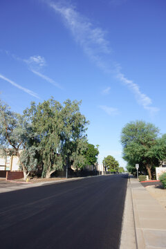 Freshly paved black asphalt street in a quiet suburban residential neighborhood under a bright blue desert sky, Phoenix, AZ