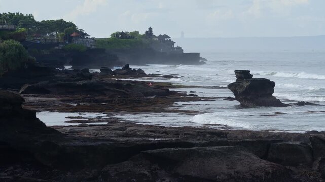 Rocky Shoreline With Distant Tanah Lot Temple, Exposed Rock Pools And Tide Patterns, Greening Clifftop And Geological Outcrops, Contemplative Coastal Scene, Tanah Lot temple, Bali, Indonesia