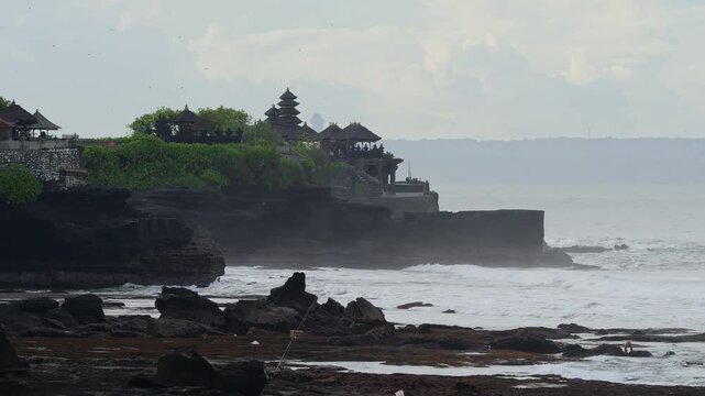 Silhouette Tanah Lot Temple Perched On Cliff Overlooking Ocean At Dusk, Multitiered Thatched Roofs, Stone Stairway, Small Figure Standing Near Edge, Misty Horizon, Gentle Waves Breaking Against Rocks,