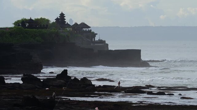 Calm Sunrise Over Tranquil Tanah Lot Temple Setting. Early Morning Mist Surrounds Silhouetted Temple On Cliff Edge. Gentle Waves And Golden Light Create Peaceful Atmosphere, Bali, Indonesia