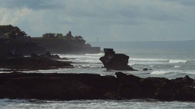 Coastal Bali Temple Silhouette Above Ocean, Misty Horizon With Layered Cliffs And Lush Green Foreground, Traditional Meru Shrine Roofs Rising From Rock Outcrop, Tranquil Sunset Tones And Spiritual